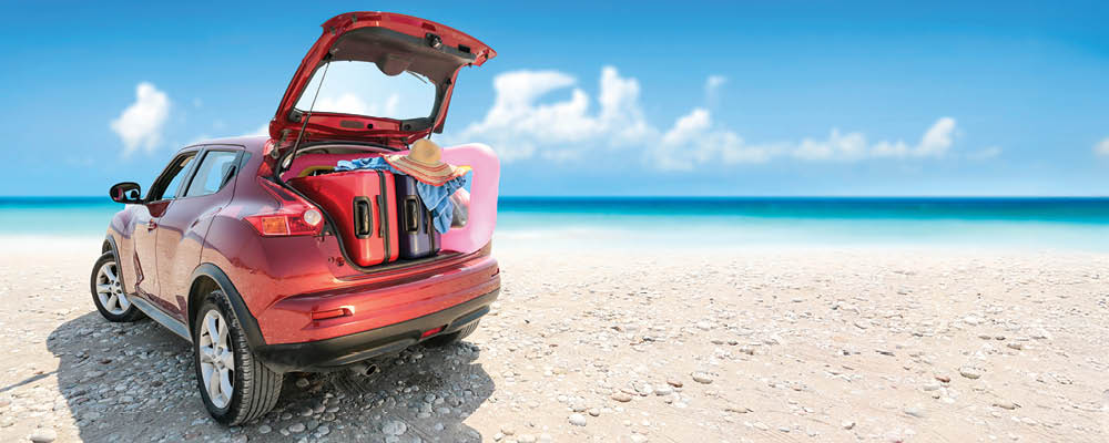 Car on the beach with trunk open and luggage in the back.
