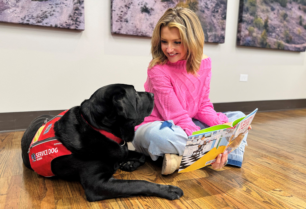 Woman reading book with her service dog.