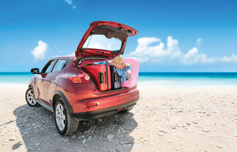 Car on the beach with trunk open and luggage in the back.