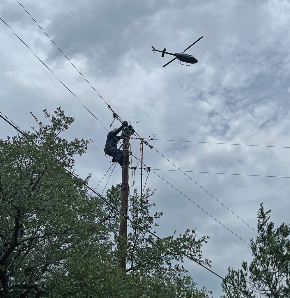 Photo of PEC lineworker on power pole with a helicopter flying over.